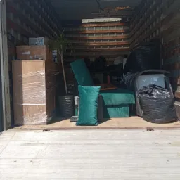 Wnętrze ciężarówki załadowane meblami, kartonami owiniętymi folią stretch, rośliną doniczkową i workami na śmieci podczas przeprowadzki.