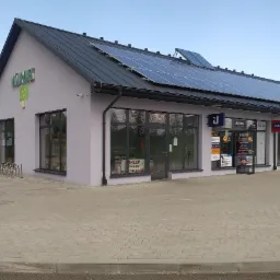 Budynek placówki partnerskiej Unilink S.A. z panelami słonecznymi na dachu i szyldami reklamowymi Warta.