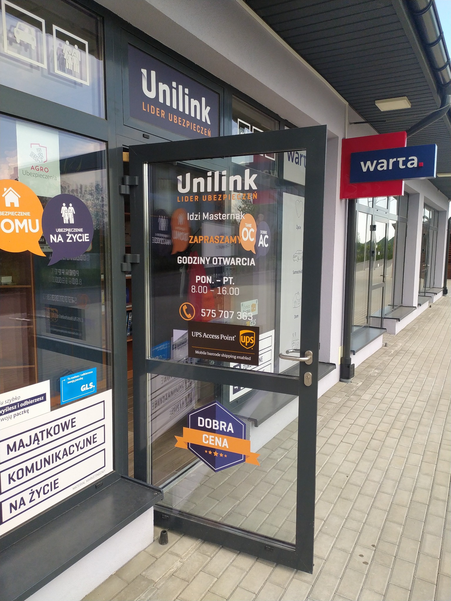 Otwarta szklana witryna placówki partnerskiej Unilink S.A. w Iwaniskach z widocznymi naklejkami informacyjnymi o ubezpieczeniach majątkowych, na życie, OC/AC oraz logo UPS i GLS.
