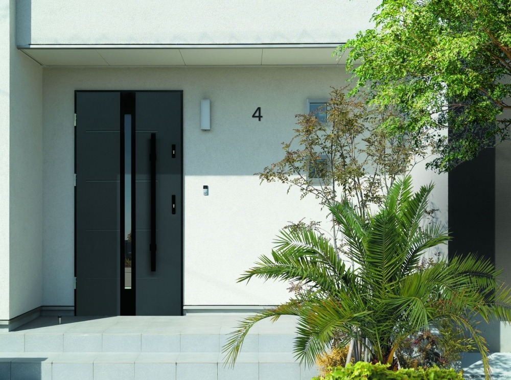 Nowoczesne, grafitowe wejście do domu z numerem '4', otoczone zielenią, z długim, pionowym uchwytem i białymi ścianami.