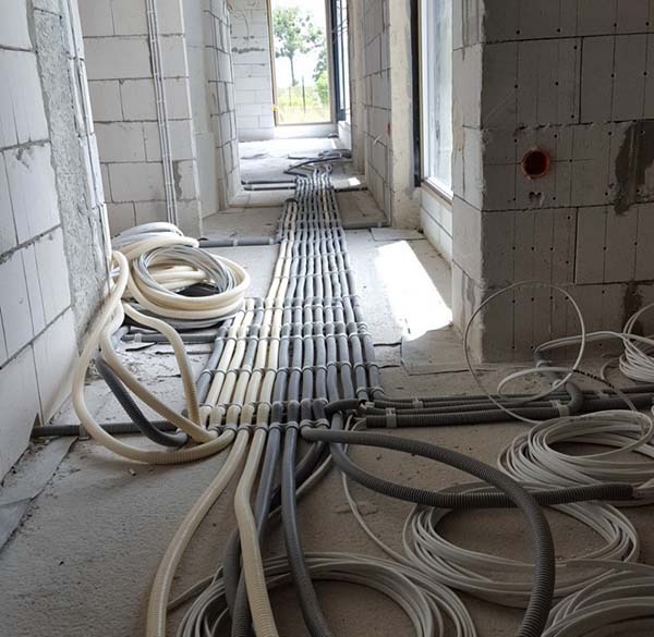 Rzędy peszli z przewodami ułożone na surowym betonie w trakcie prac w budynku w stanie deweloperskim, widoczne puszki instalacyjne w ścianach z betonu komórkowego.