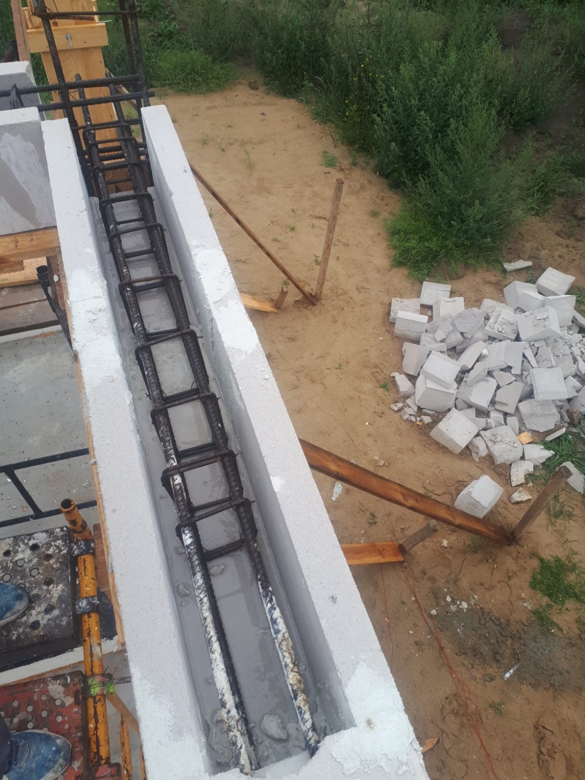 Wypełniony betonem wieniec zbrojeniowy w bloczkach szalunkowych na fundamencie, widoczne fragmenty rusztowania i porozrzucane bloczki.