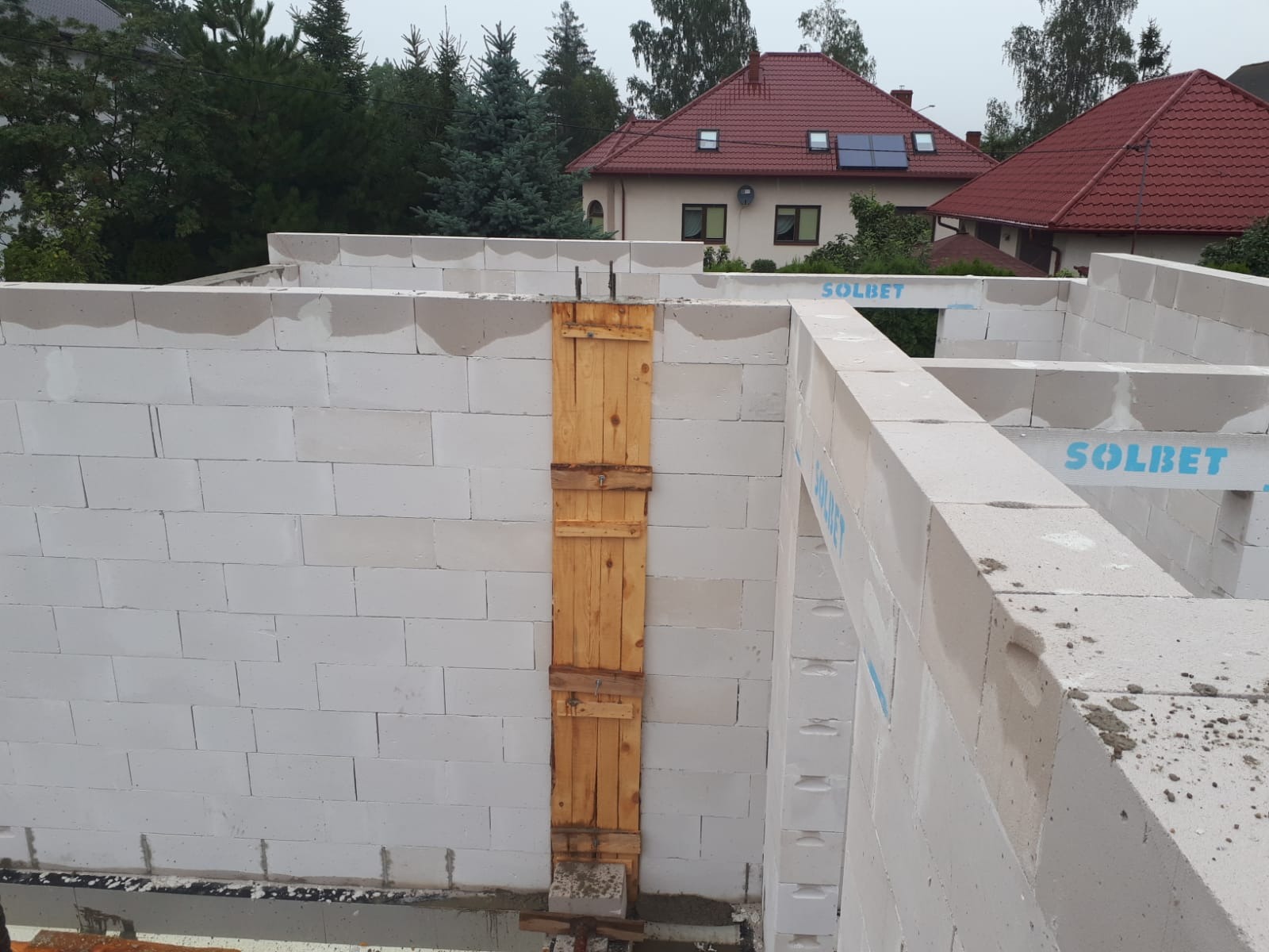 Wznoszenie ścian domu z betonu komórkowego Solbet, z widocznym zabezpieczeniem pionowym z desek i stempli, przygotowanym do izolacji fundamentów.