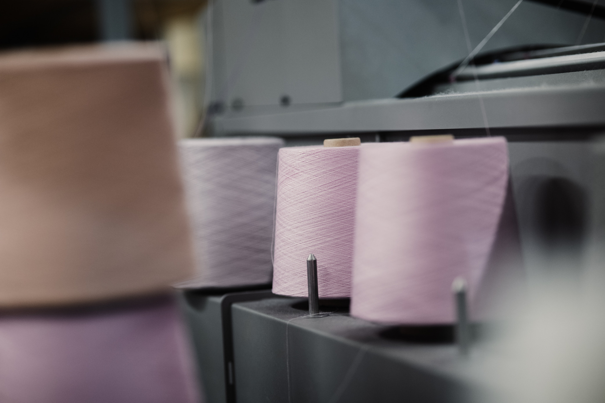 Rzędy szpul z delikatną, różową przędzą na nowoczesnej maszynie dziewiarskiej, z ostrością skupioną na środkowej szpuli i subtelnym rozmyciem tła.