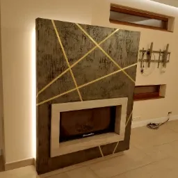 Obudowa kominka z szarego betonu architektonicznego z geometrycznymi, złotymi wstawkami, podświetlana listwą LED, w nowoczesnym salonie.