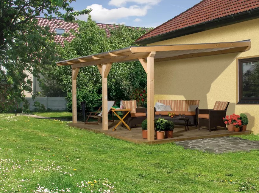 Zadaszona, otwarta konstrukcja z drewna, pełniąca funkcję relaksacyjną w ogrodzie, z drewnianym podestem, meblami ogrodowymi i roślinami w donicach, przylegająca do ściany domu z oknem.