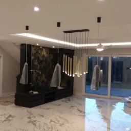 Nowoczesne wnętrze z marmurową posadzką, oświetleniem punktowym i wiszącymi lampami, niektóre jeszcze zabezpieczone folią ochronną, sugerujące prace wykończeniowe.