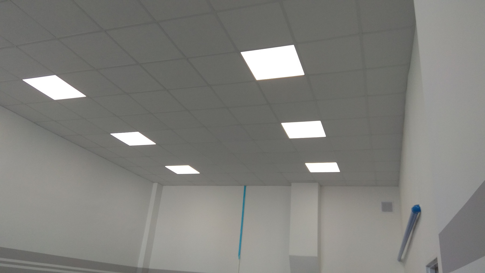 Sufit podwieszany z zamontowanymi kwadratowymi panelami LED, widok z dołu, surowe wnętrze z białą ścianą i kolumną.