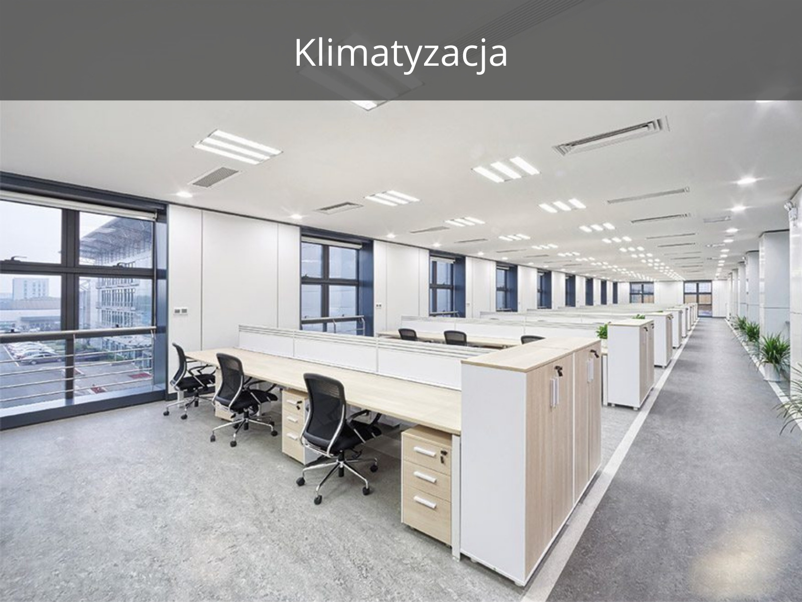 Nowoczesne biuro z systemem wentylacji sufitowej, widoczne kratki wentylacyjne w suficie, biurka z krzesłami i duże okna z widokiem na miasto.