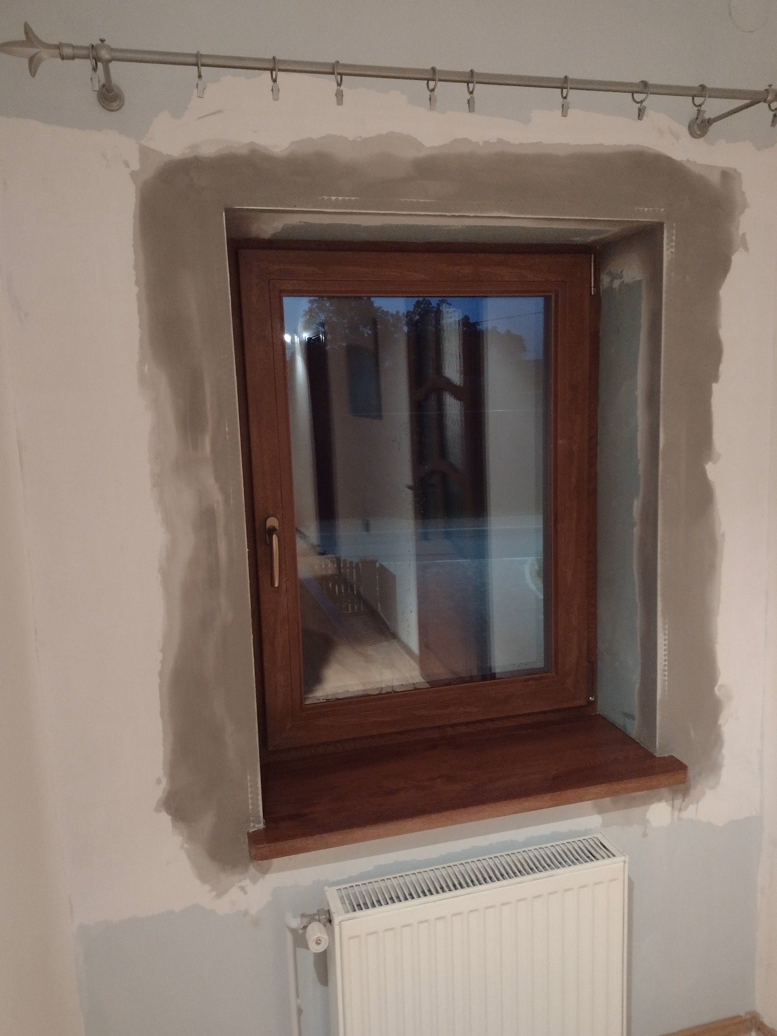 Drewniane okno po montażu, z widocznymi śladami szpachlowania na ścianie i grzejnikiem pod parapetem.