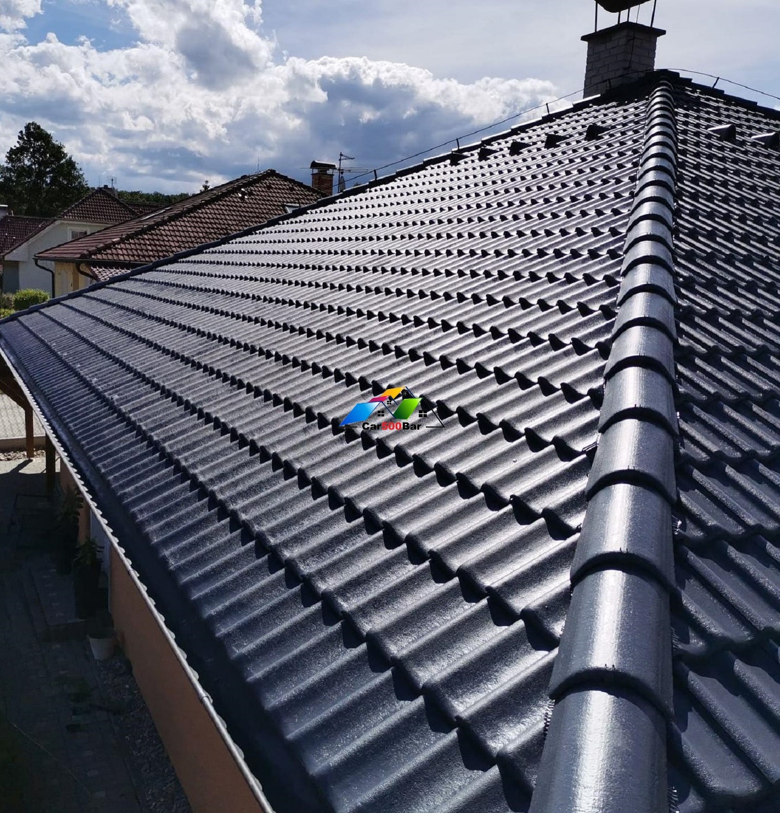 Ciemnoszary dach z dachówki ceramicznej, widok z góry na tle błękitnego nieba z chmurami, widoczne kominy sąsiednich domów.