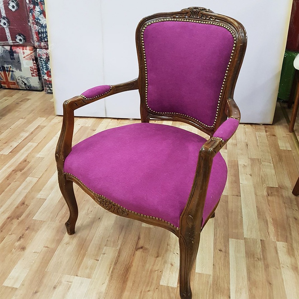 Odrestaurowany fotel w stylu Ludwika Filipa, z nową, fioletową tapicerką i ozdobnymi gwoździami, stojący na drewnianej podłodze.