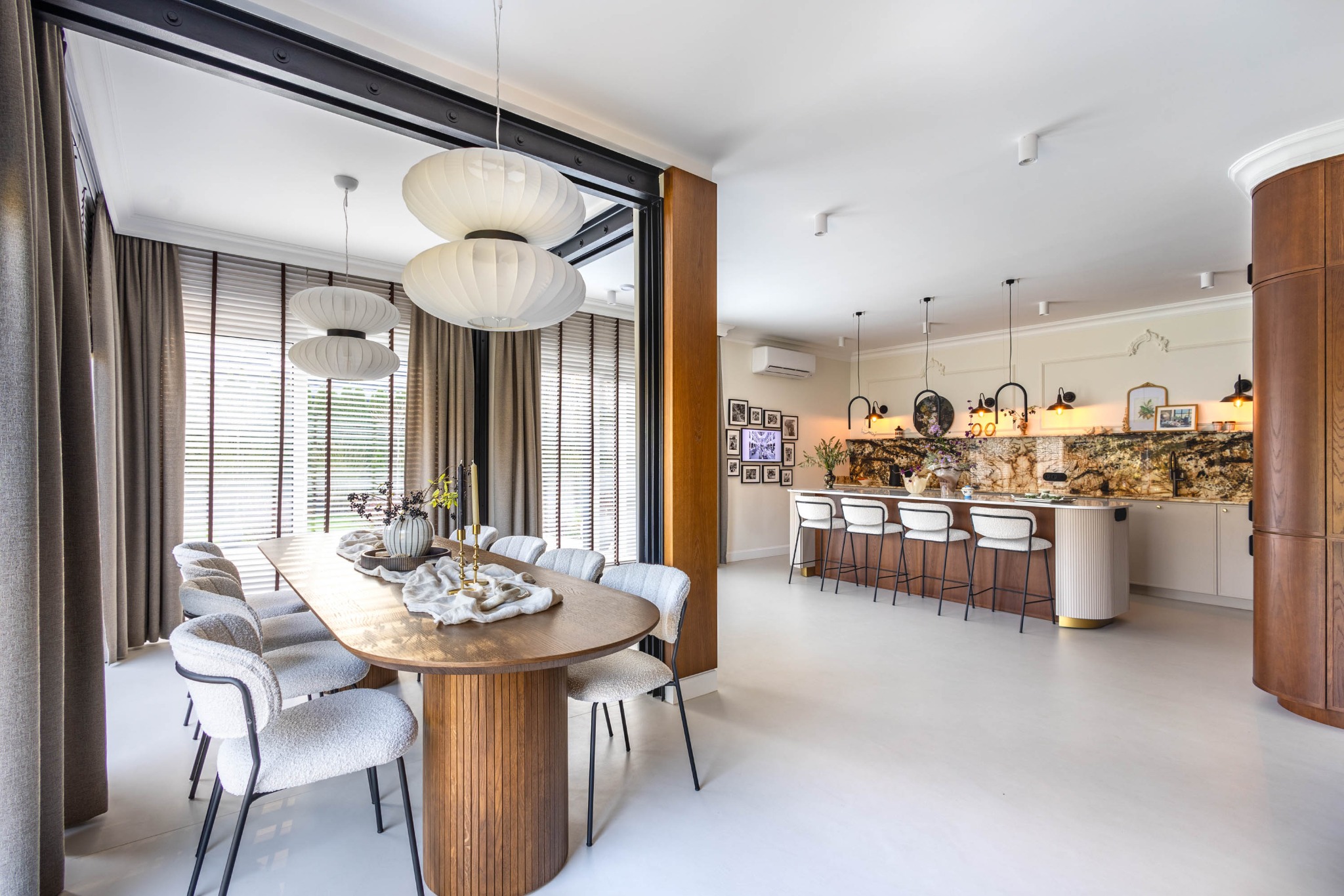 Eleganckie wnętrze: jadalnia z owalnym stołem i krzesłami boucle, otwarta na kuchnię z barkiem. Naturalne światło, drewniane akcenty i designerskie lampy.