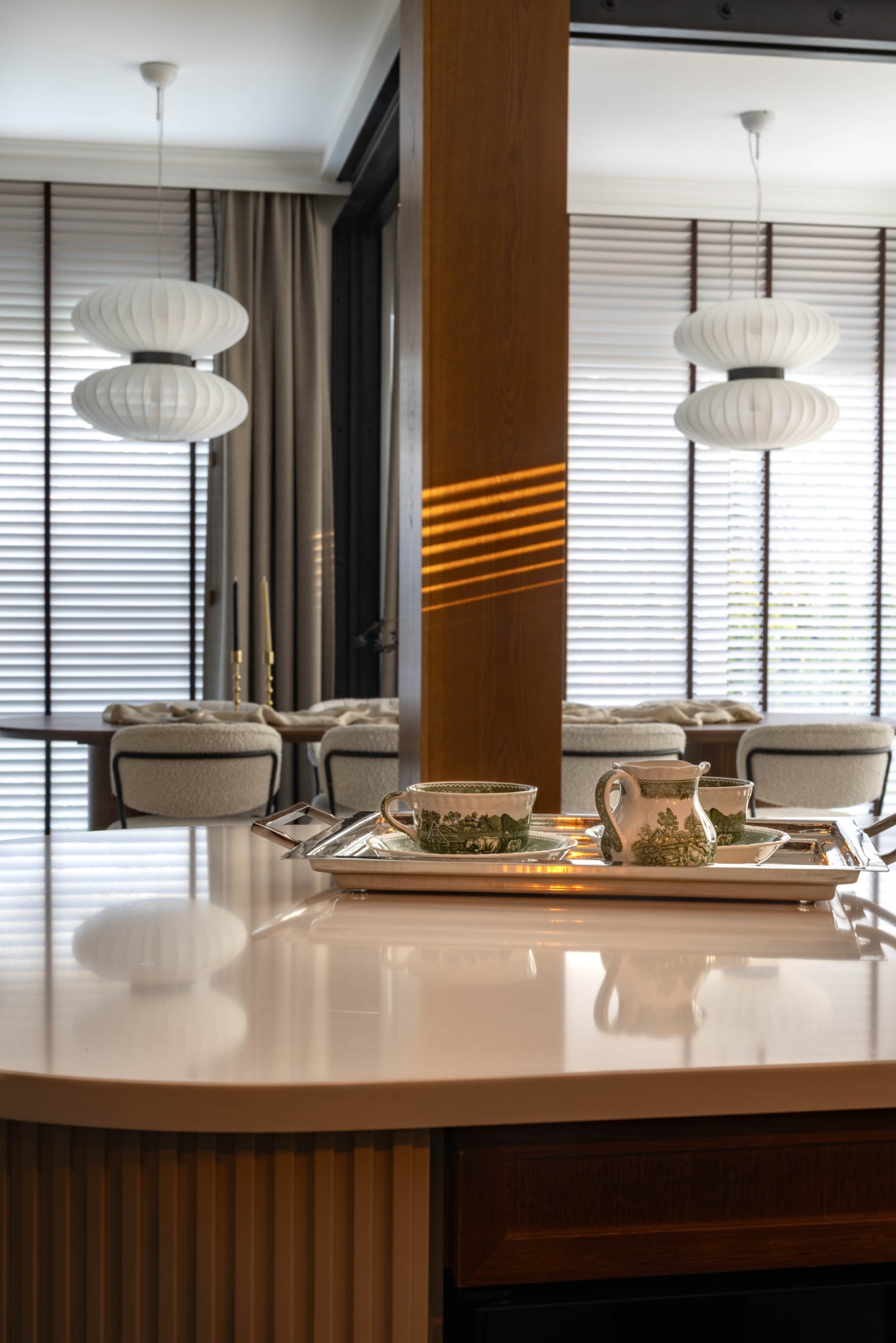 Stylowe wnętrze: filiżanki i dzbanek na srebrnej tacy na blacie, w tle okno z żaluzjami i lampy w kształcie kuli. Ciepłe światło słoneczne na drewnianym słupie.