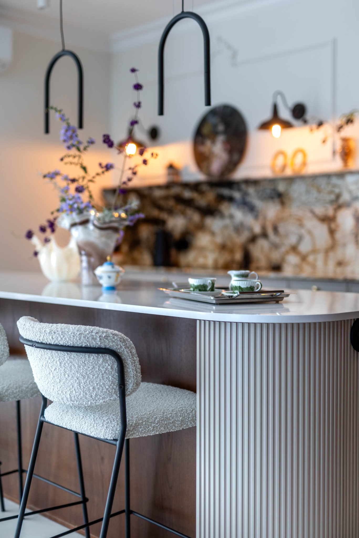 Nowoczesna kuchnia z wyspą: krzesła barowe z tkaniny boucle, marmurowy blat, dekoracje i oświetlenie. Ujęcie z bliska, detale wykończenia.