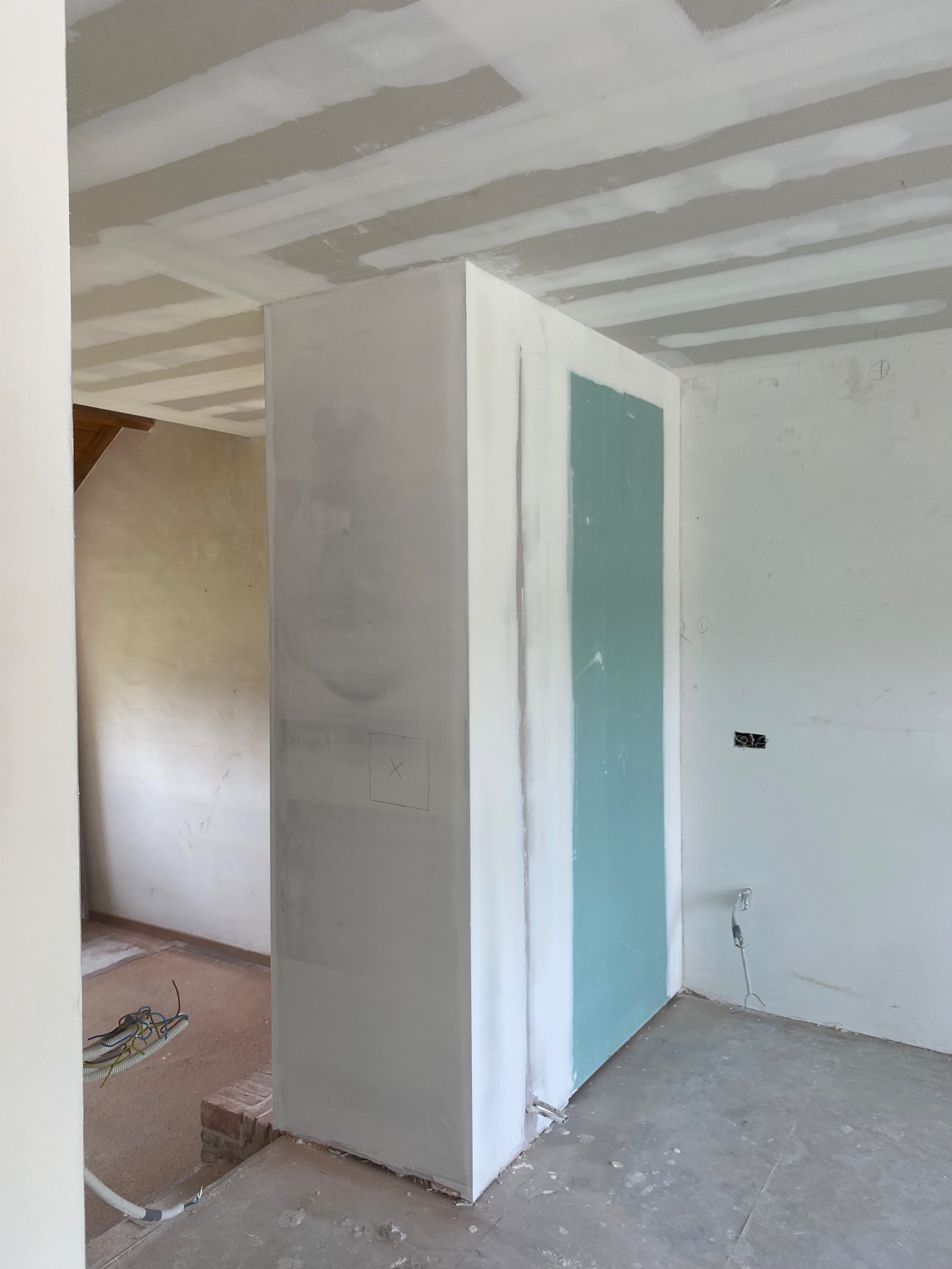 Wnętrze w trakcie prac wykończeniowych: ściany z częściowo położoną płytą gipsowo-kartonową, widoczne profile na suficie, instalacja elektryczna. Na ścianie zaznaczony ołówkiem kwadrat.