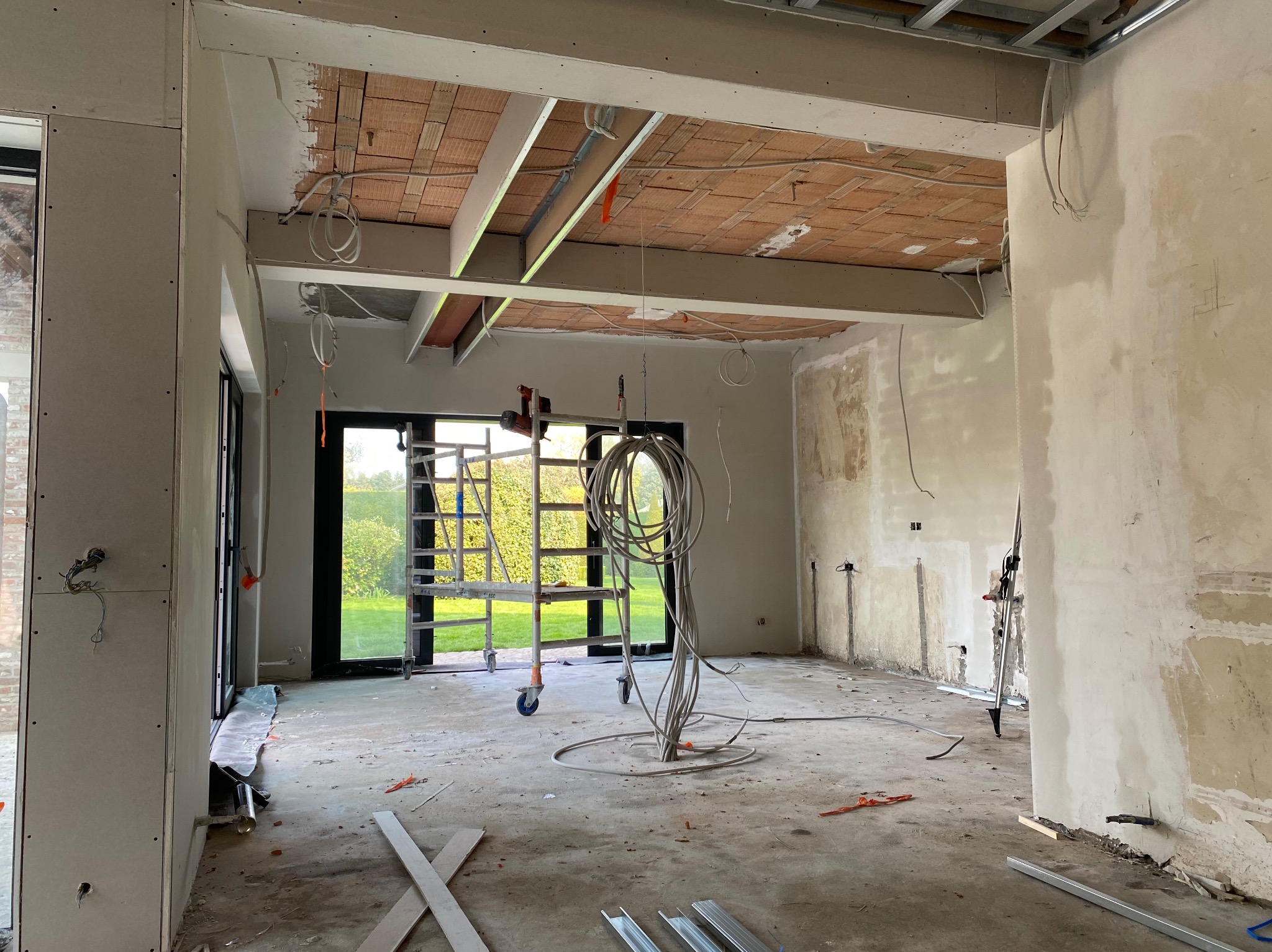 Wnętrze w trakcie prac wykończeniowych: widoczne ściany przygotowane do montażu płyt, częściowo zamontowana konstrukcja sufitu podwieszanego z widoczną instalacją elektryczną, rusztowanie...