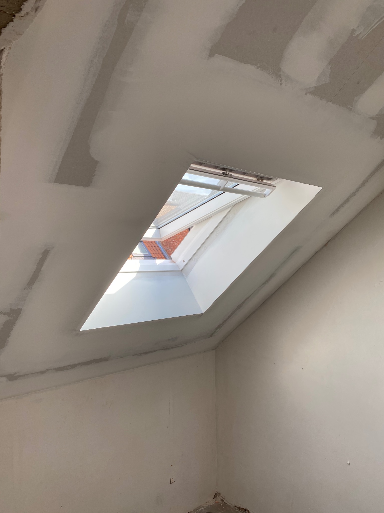 Poddasze z oknem dachowym, ściany i sufit w trakcie szpachlowania, widoczne łączenia płyt karton-gips.