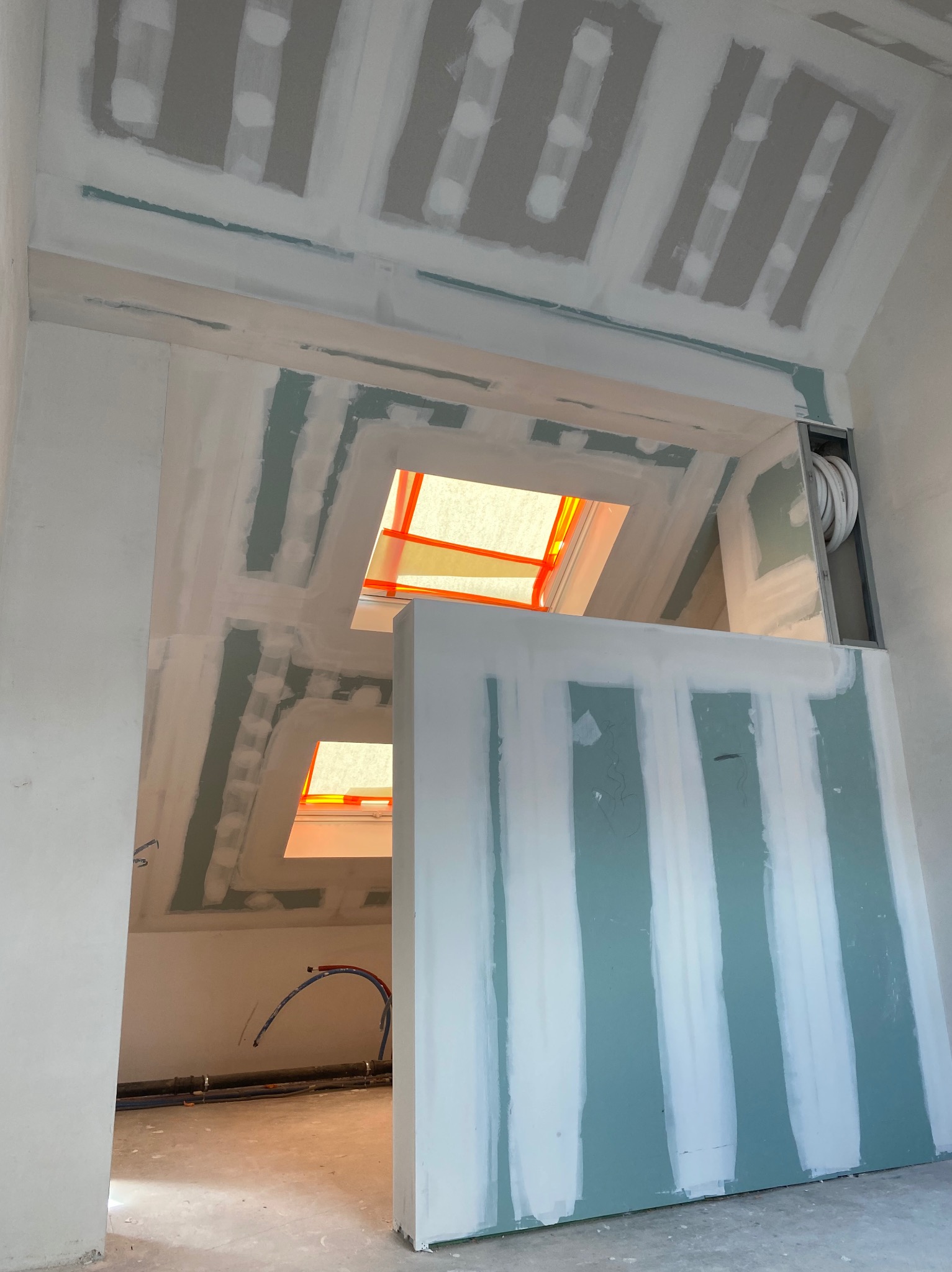 Montaż płyt na poddaszu z oknami dachowymi, widoczne szpachlowanie łączeń, instalacja elektryczna i hydrauliczna w tle.