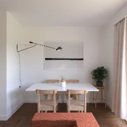 Jasne wnętrze jadalni z białym stołem, drewnianymi krzesłami, lampą na ścianie i minimalistycznym obrazem w tle.