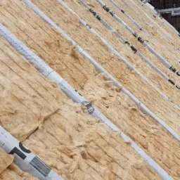 Poddasze z widoczną izolacją termiczną z wełny mineralnej, zabezpieczoną folią z nadrukiem, ułożoną między krokwiami dachu.