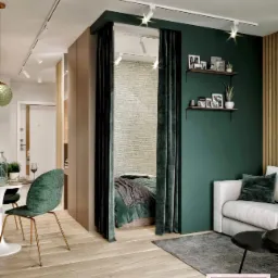 Nowoczesne wnętrze z wydzieloną strefą sypialnianą za pomocą ciemnozielonych zasłon, drewniana podłoga, biała sofa i ściana w odcieniu butelkowej zieleni z półkami na dekoracje.
