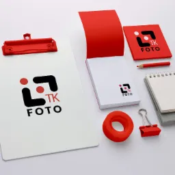 Zestaw materiałów biurowych z logo TK FOTO: notatniki, podkładka, ołówek i klips w kolorze czerwonym, ułożone na białym tle.