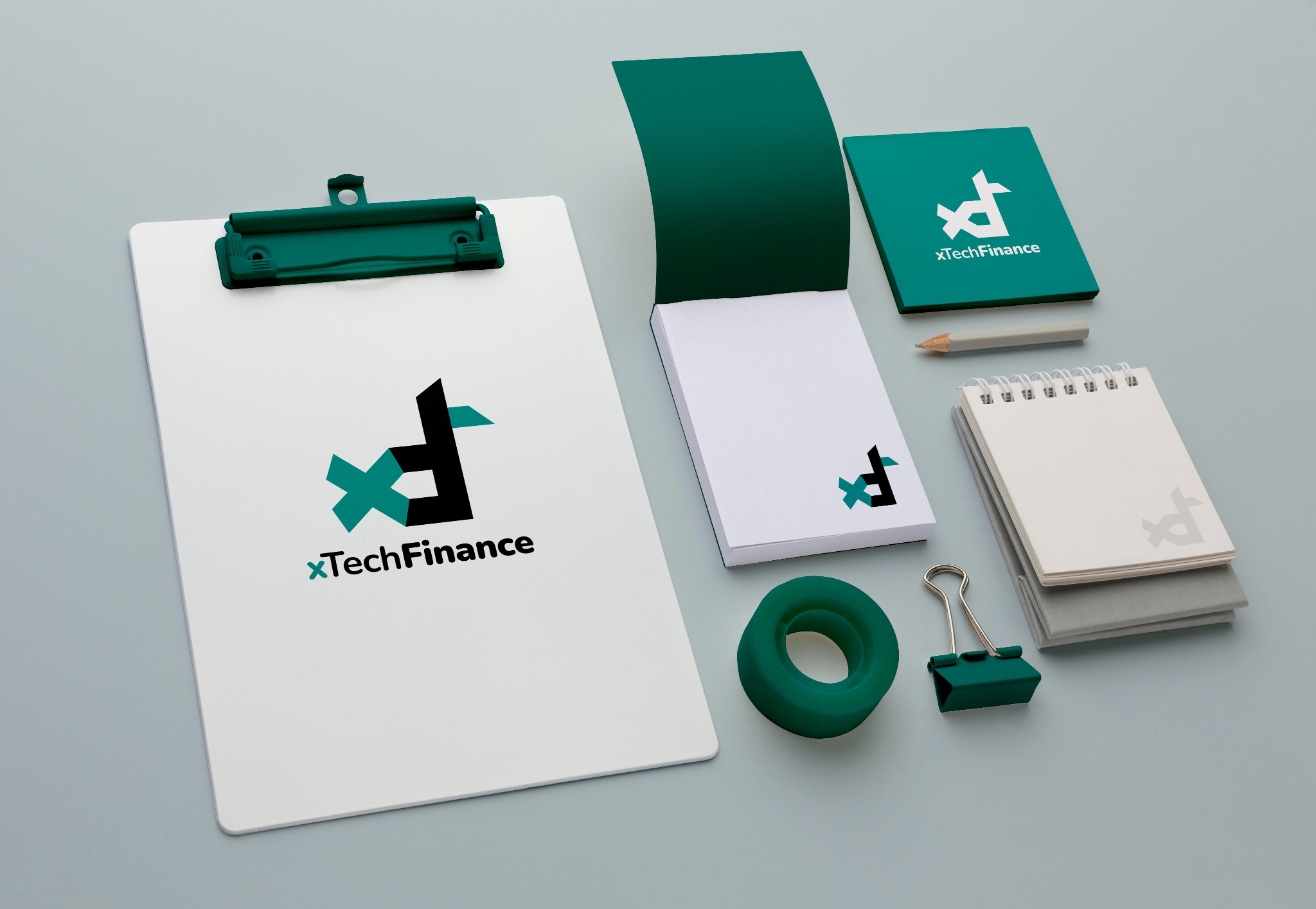 Zestaw materiałów biurowych z logo XTechFinance: notatnik, bloczek, podkładka z klipsem, ołówek, gumka i spinacz biurowy w odcieniach bieli i zieleni na gładkim, szarym tle.