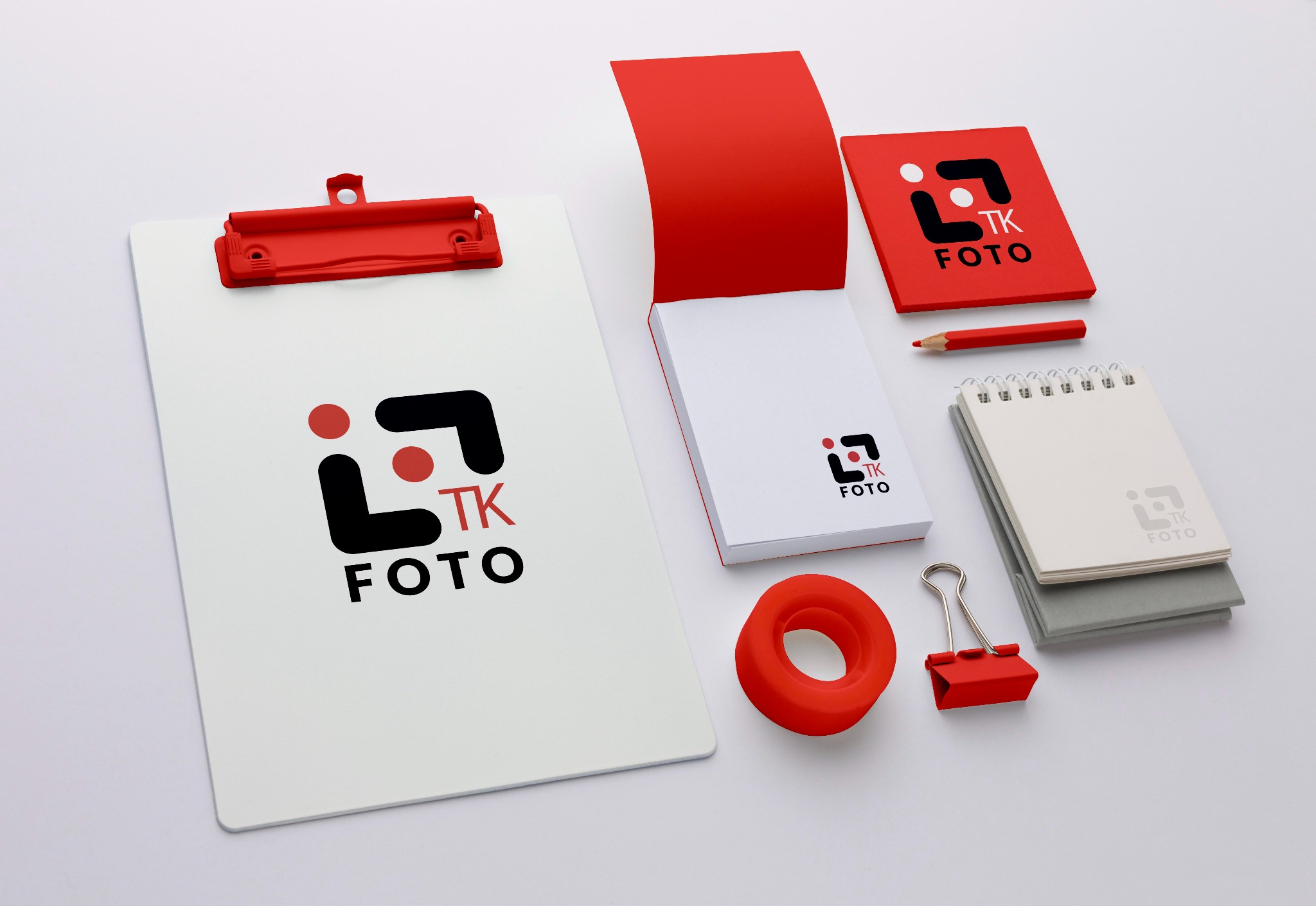 Zestaw materiałów biurowych z logo TK FOTO: notatniki, podkładka, ołówek i klips w kolorze czerwonym, ułożone na białym tle.