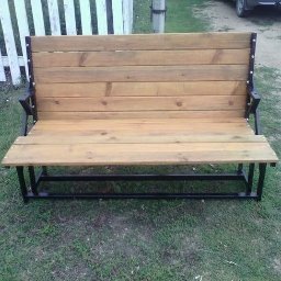 KUE PROJEKT SP. Z O.O. - Drewniana ławka ogrodowa z czarną metalową konstrukcją, ustawiona na trawie przed białym płotem.