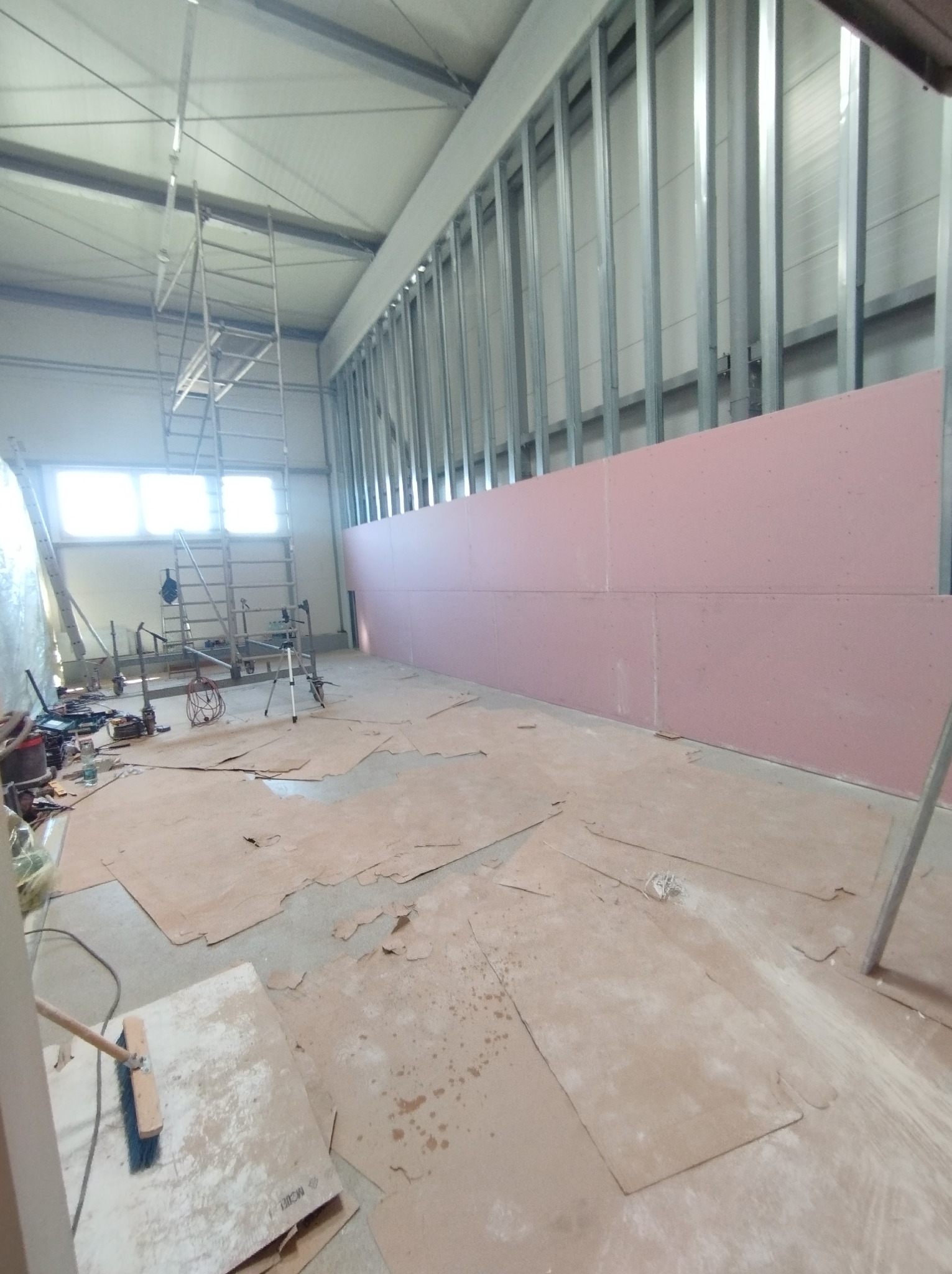 Montaż różowych płyt kartonowo-gipsowych na metalowym stelażu w przestronnym, jasnym pomieszczeniu; widoczny rozstawiony ruszt i narzędzia.