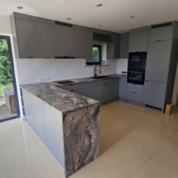 KAMILA MOSPINEK - MEBLE KONCEPT - Szara kuchnia na wymiar z marmurowym blatem. Widok na zewnątrz przez duże okno. Nowoczesny design, minimalistyczne fronty, oświetlenie punktowe.