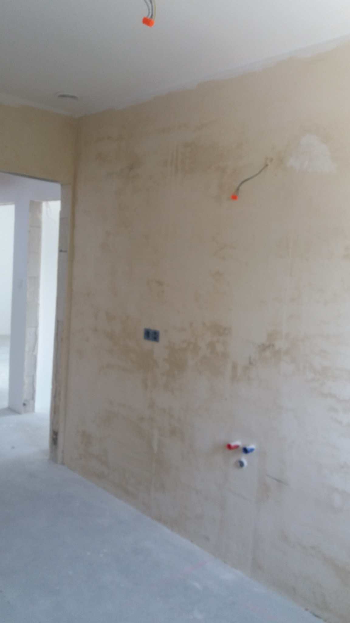 Ściana wewnętrzna po nałożeniu warstwy tynku, widoczne przygotowane instalacje elektryczne i wodne, surowy stan wykończenia.