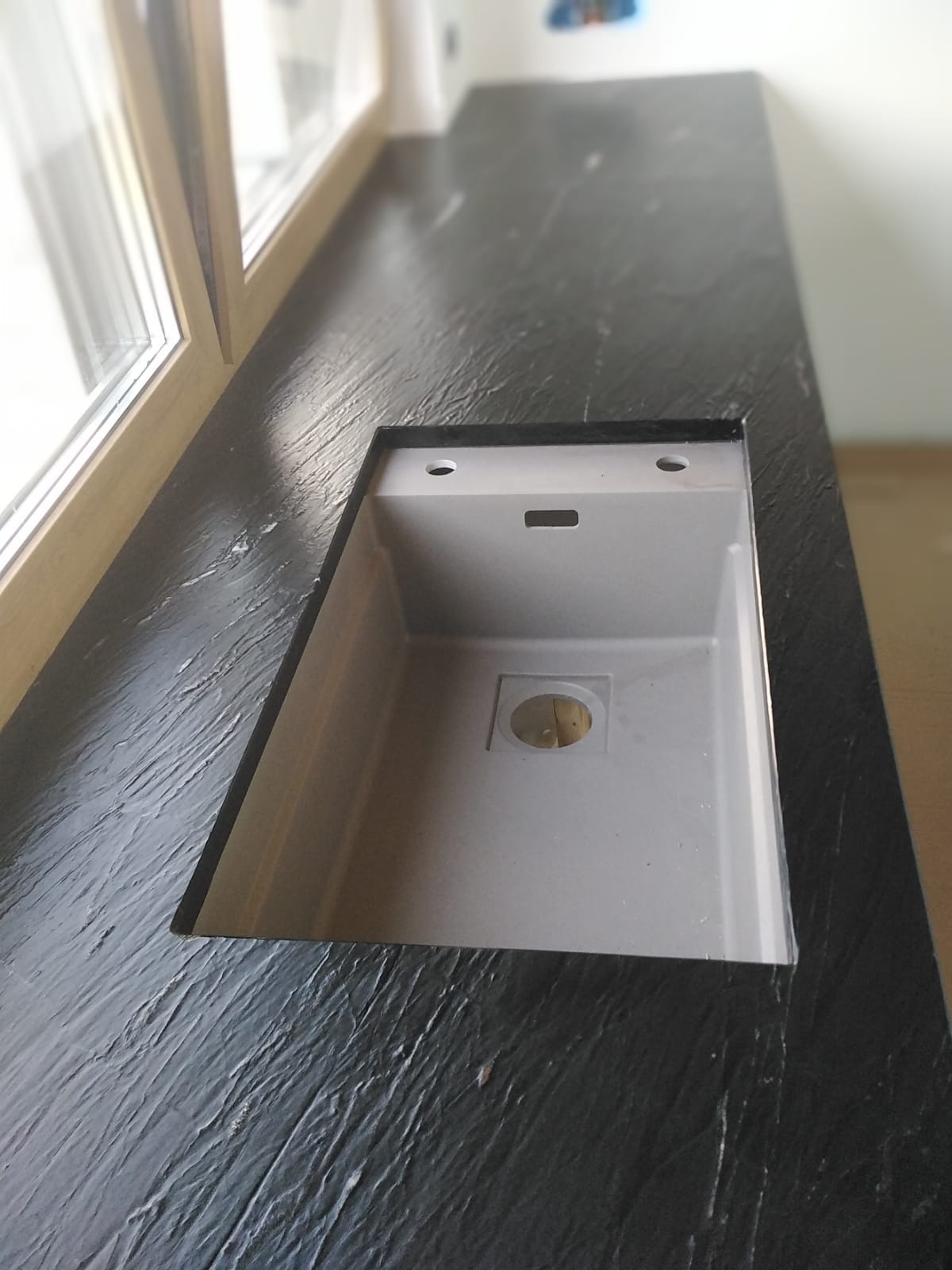 Czarny blat z wyciętym otworem na zlew, widoczna faktura materiału przypominająca łupane skały.