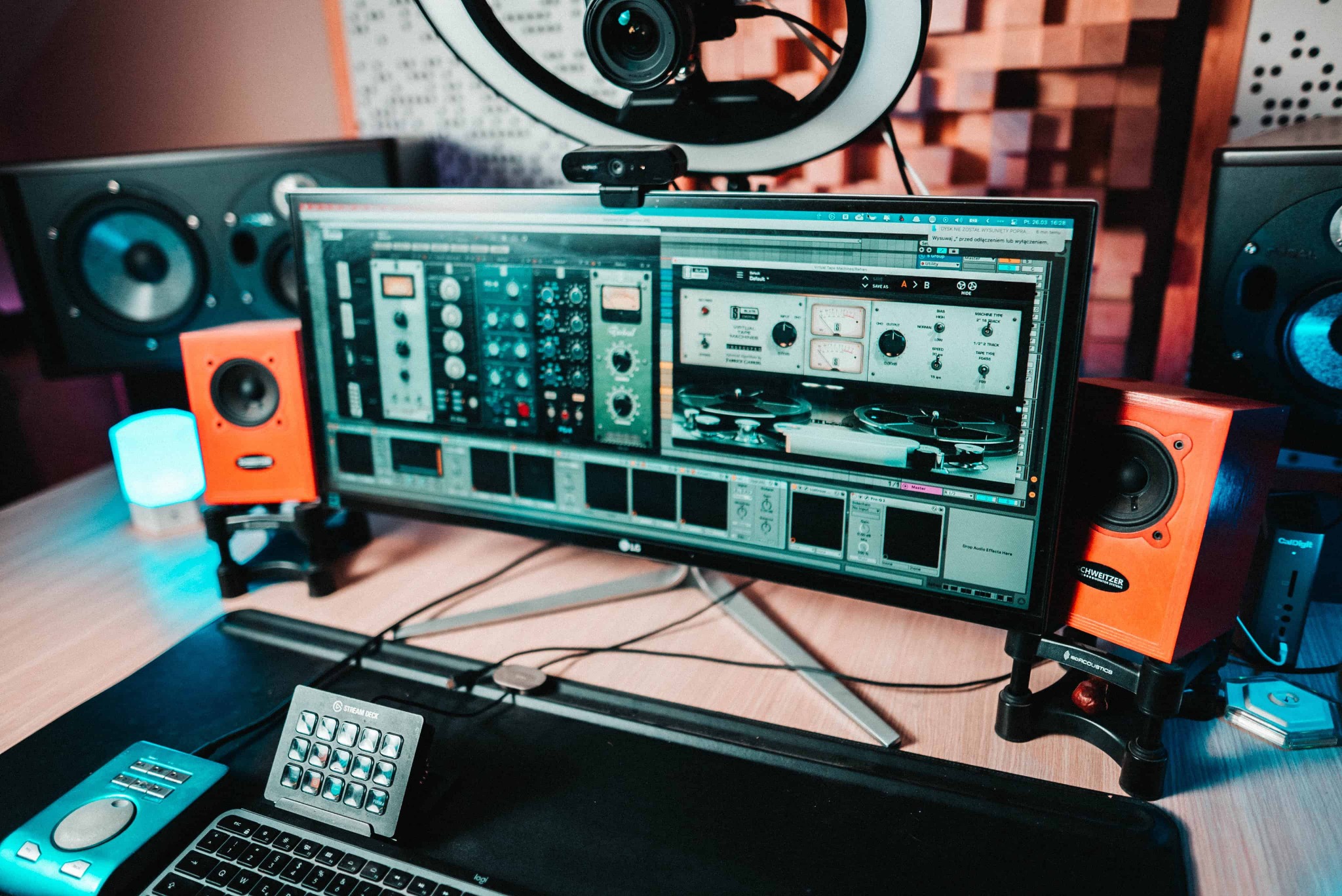 Monitor wyświetlający oprogramowanie do edycji dźwięku z wirtualnymi efektami, otoczony studyjnymi monitorami odsłuchowymi i lampą pierścieniową, na biurku z klawiaturą i kontrolerem Stream Deck.