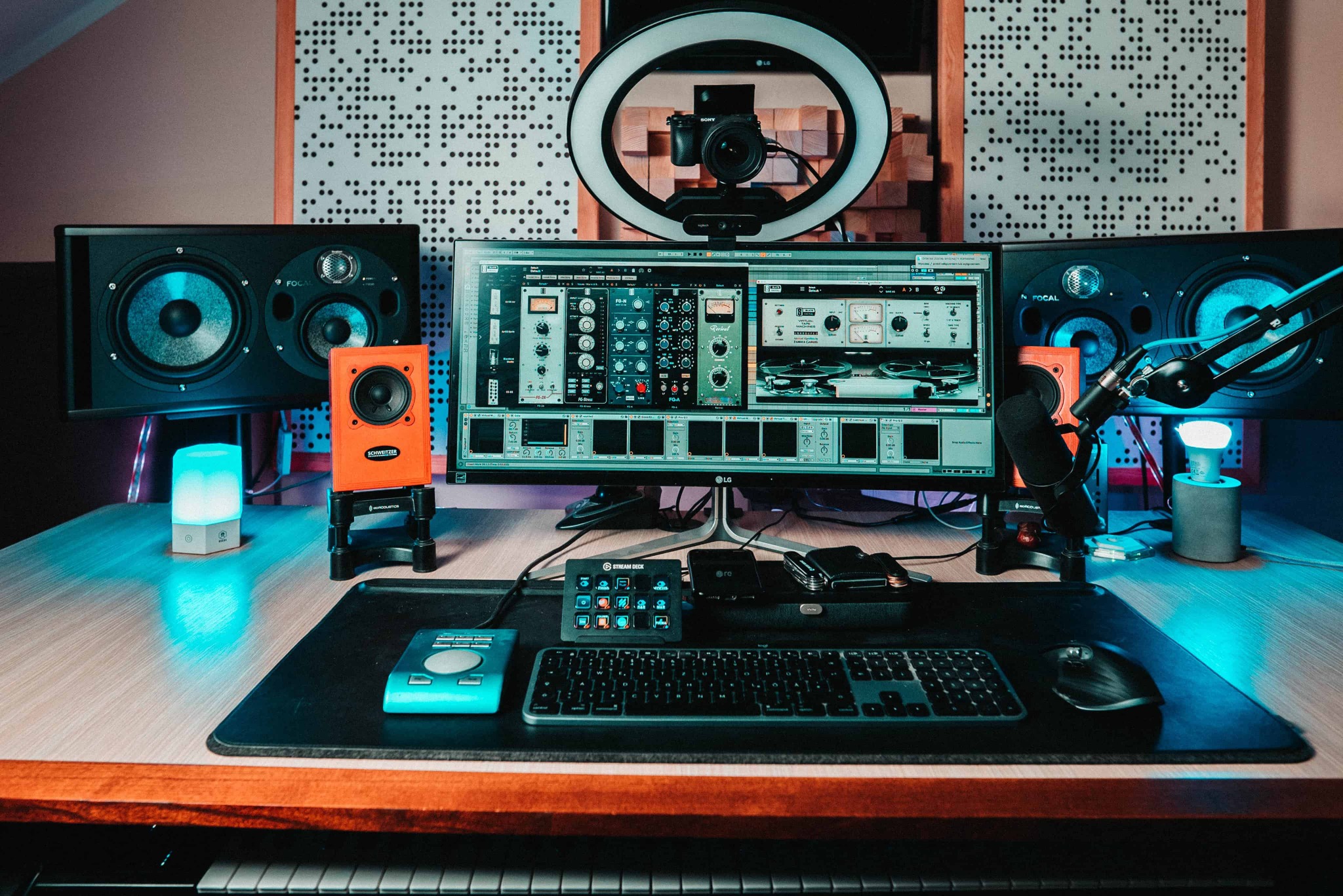 Biurko z profesjonalnym sprzętem audio: monitory studyjne Focal, mały głośnik Schweitzer, mikrofon, klawiatura MIDI, kontroler Stream Deck, oświetlenie LED i monitor z otwartym programem DAW.