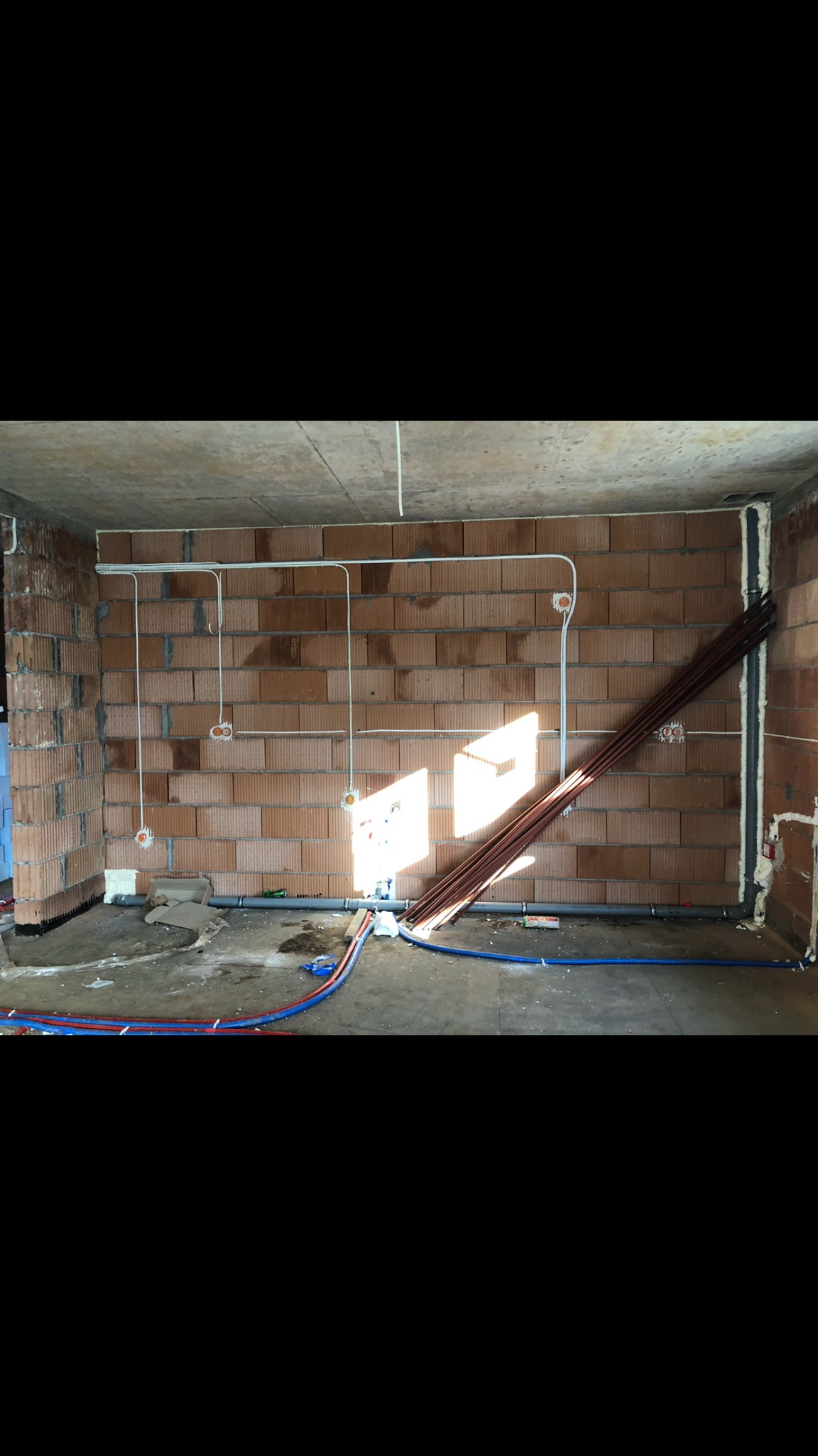 Instalacja elektryczna i hydrauliczna w surowym wnętrzu budynku w Krakowie, widoczne przewody w ścianach z cegły oraz rury na podłodze.