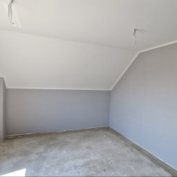 KRIS MAR - Świeżo pomalowane na szaro poddasze z białym sufitem, widoczne gniazdka elektryczne bez osprzętu i surowa podłoga przed wylewką.