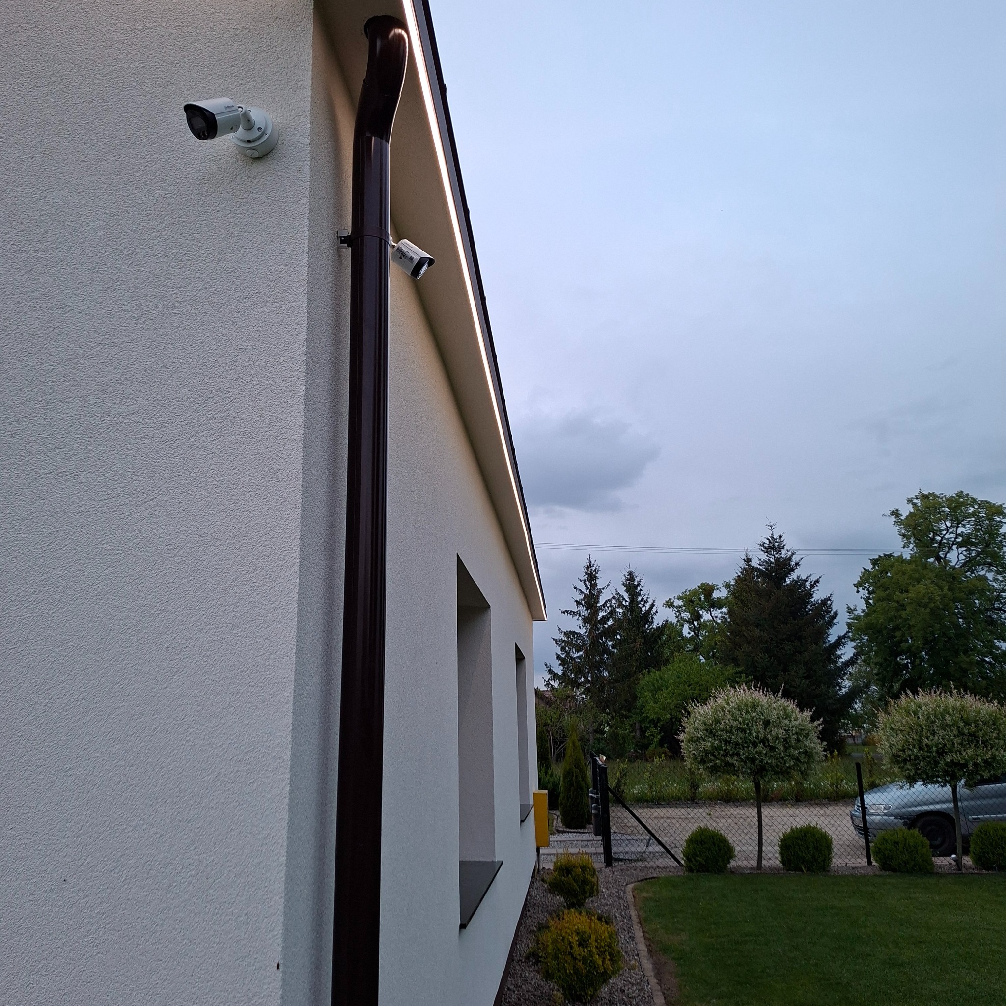 Elewacja domu z zamontowanym monitoringiem (dwie kamery) i oświetleniem LED pod dachem, widok z boku.