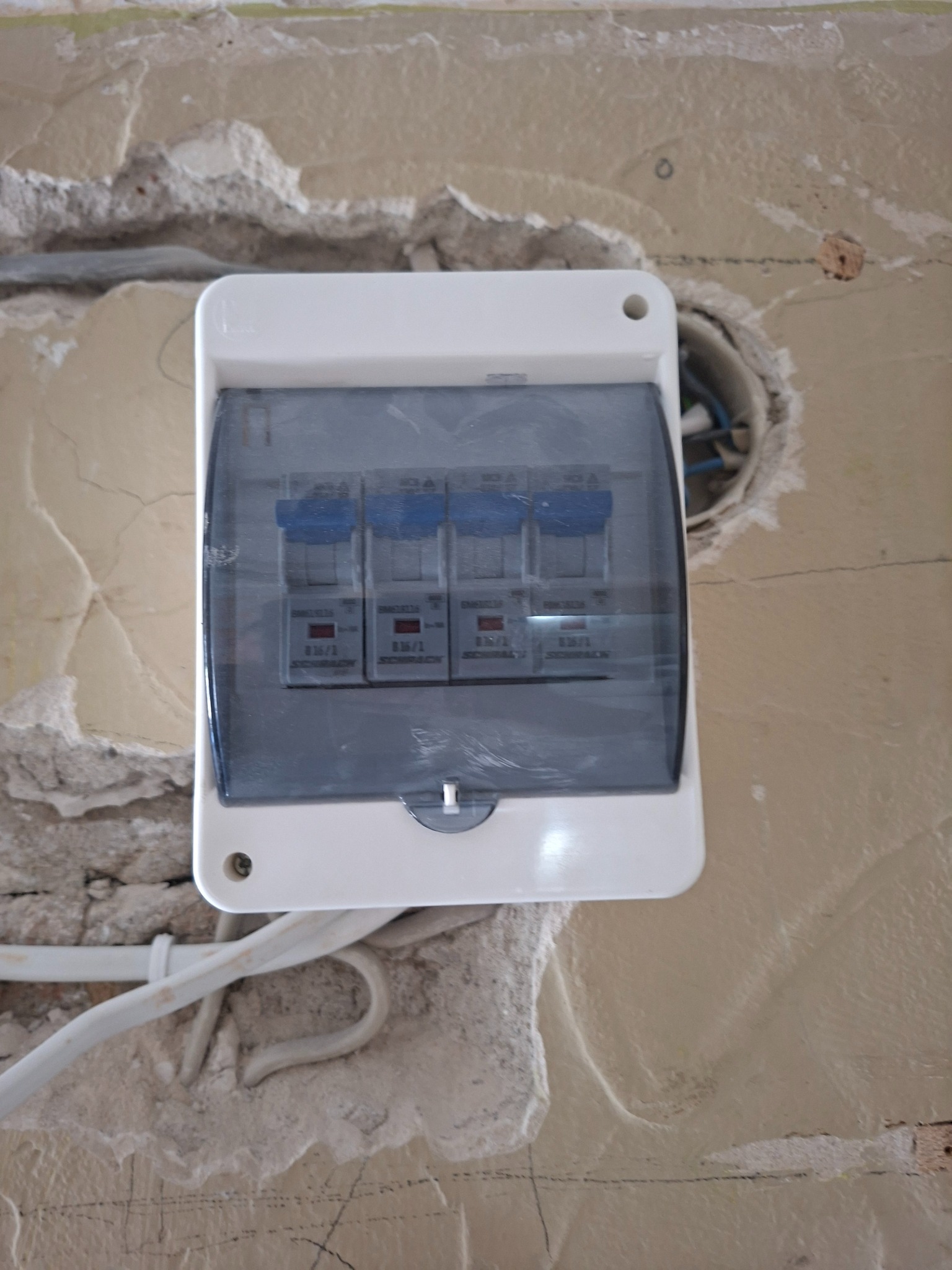 Zamontowana skrzynka bezpiecznikowa z widocznymi czterema bezpiecznikami na surowej ścianie z wystającymi przewodami elektrycznymi.