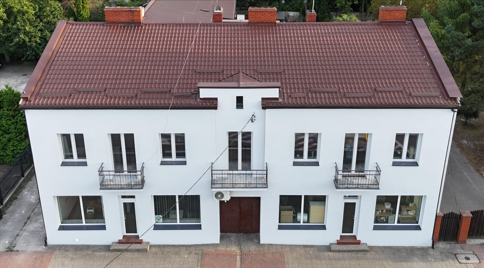 Dwukondygnacyjny budynek po remoncie elewacji z nową, brązową dachówką, białymi ścianami i balkonami z czarną balustradą, widziany z góry.