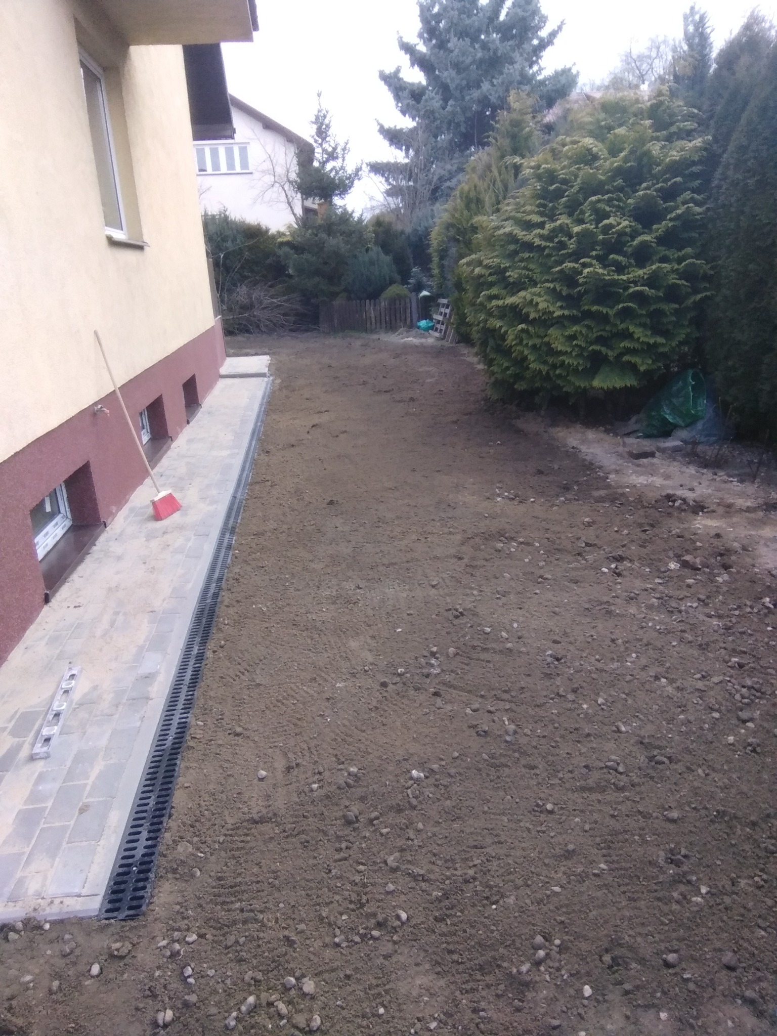 Przygotowanie terenu pod ocieplenie ścian w Piastowie: widok na odsłonięty fundament, ułożoną kostkę brukową z odpływem liniowym i leżącą miotłę przy ścianie budynku.