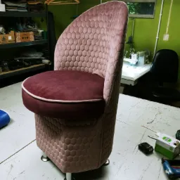 Gotowe krzesło tapicerowane w odcieniach różu i bordo, z geometrycznym wzorem plastra miodu, stojące w warsztacie z maszyną do szycia w tle.