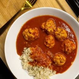 Marita Bambrowicz Dietetyka - Porcja pulpetów w sosie pomidorowym z ryżem brązowym, podana na białym talerzu, z widocznym złotym widelcem na drewnianym tle.