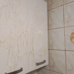 Filip Jagodziński - Zabrudzona szafka kuchenna i płytki ścienne z widocznymi zaciekami i plamami. Widoczne metalowe uchwyty szafki. Potrzeba gruntownego czyszczenia.