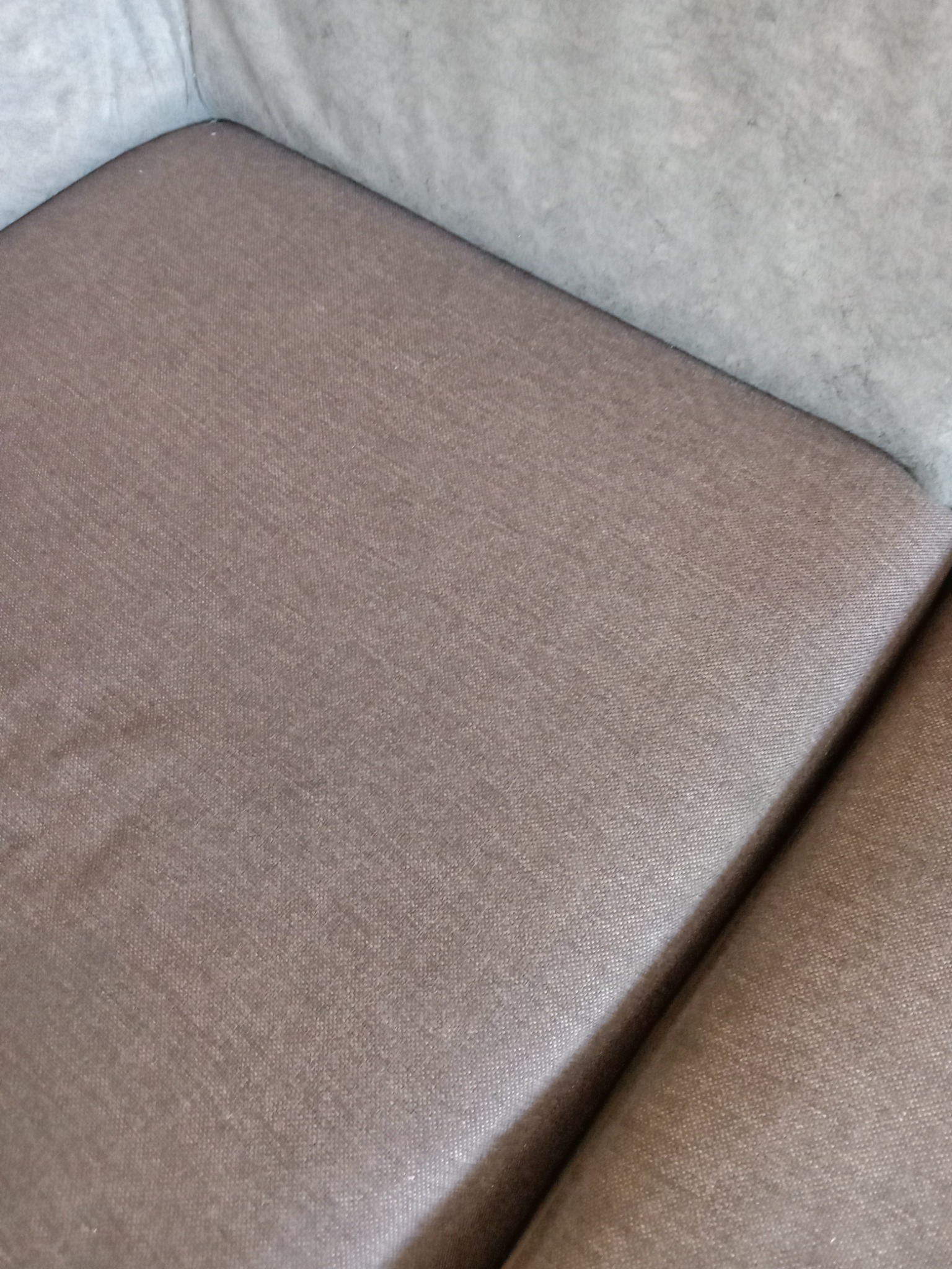 Fragment brązowej tapicerki kanapy z widoczną strukturą materiału po czyszczeniu, z szarym elementem w tle.
