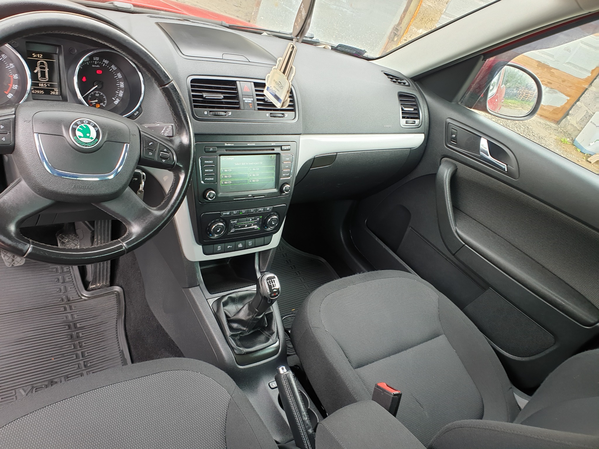 Wnętrze samochodu Skoda Yeti: deska rozdzielcza z nawiewami, radioodtwarzaczem i zawieszką zapachową, kierownica z logo marki, czarne fotele z czerwonymi pasami bezpieczeństwa, gumowe dywaniki.