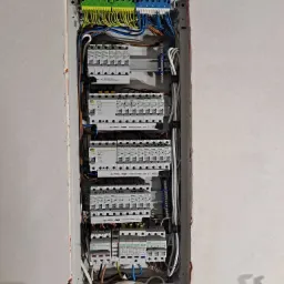 Rozdzielnica elektryczna wnękowa z zamontowanymi bezpiecznikami, listwami zaciskowymi i okablowaniem, widoczna na tle surowej ściany.