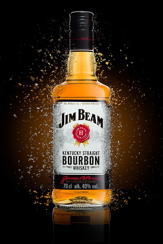 Butelka bourbonu Jim Beam, pokryta kroplami, otoczona drobnymi, złotymi odłamkami na czarnym tle z gradientem.