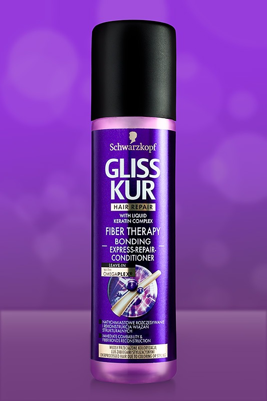 Butelka fioletowego sprayu Gliss Kur Fiber Therapy do włosów zniszczonych koloryzacją lub zabiegami stylizacyjnymi na rozmytym fioletowym tle.